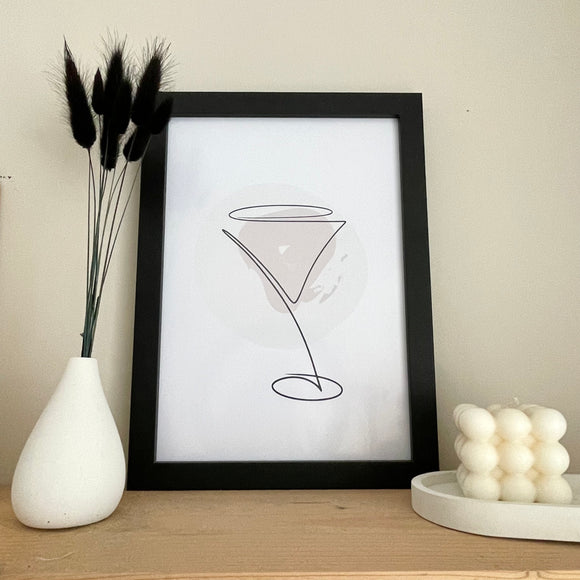 Minimalist line drawing martini wine glass wall print art. Neutral colour behind. A4 in black frame. Bubble candle to the right, white concrete bud vase with black bunny tails to the left