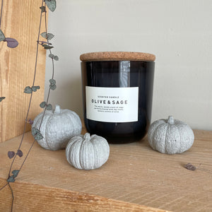 Set of 3 white concrete pumpkins sitting on a shelf next to a white candle. Autumn home decor