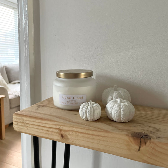 Set of 3 white concrete pumpkins sitting on a shelf next to a white candle. Autumn home decor