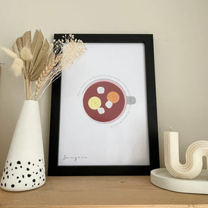 Minimalist sangria recipe cocktail print. Jug from above with sangria recipe around the edge. A4 in black frame. Sculpture candle to the right, Dalmatian design vase with palm dried flower bouquet to the left 